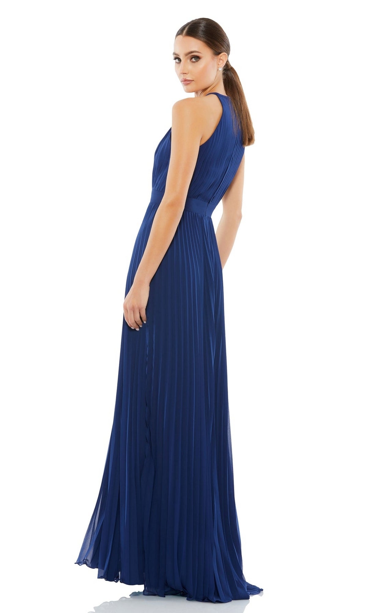 A woman with her hair in a low ponytail stands facing away against a white background, wearing the sleeveless, floor-length Long Formal Dress 12496 by Mac Duggal with pleated detailing.